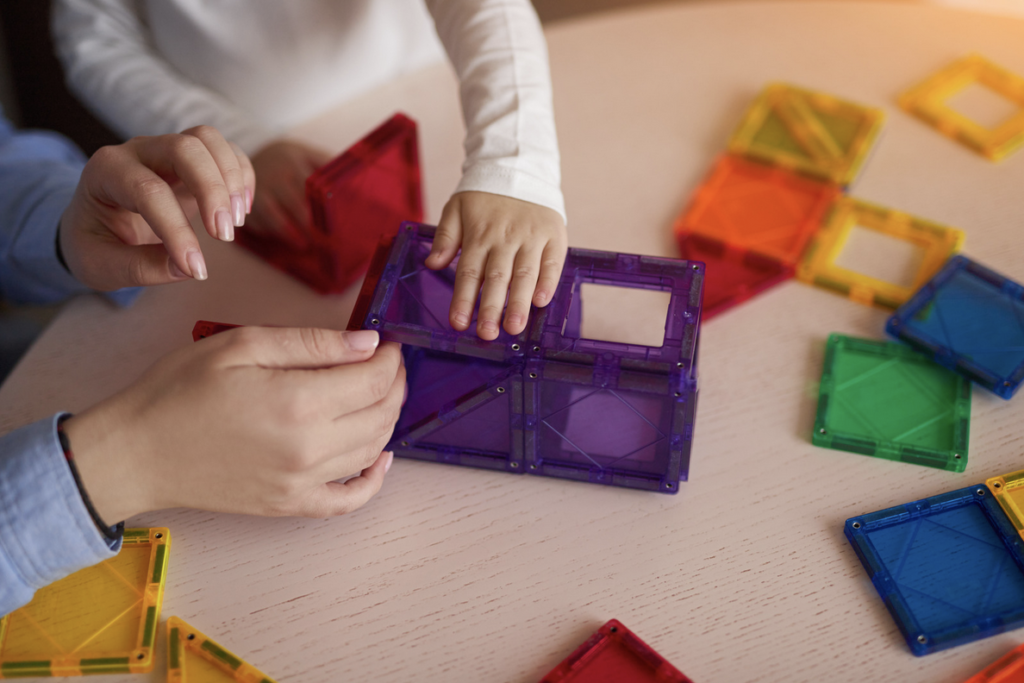 Image of parent and child playing with magnetic tiles, building a rectangular structure.