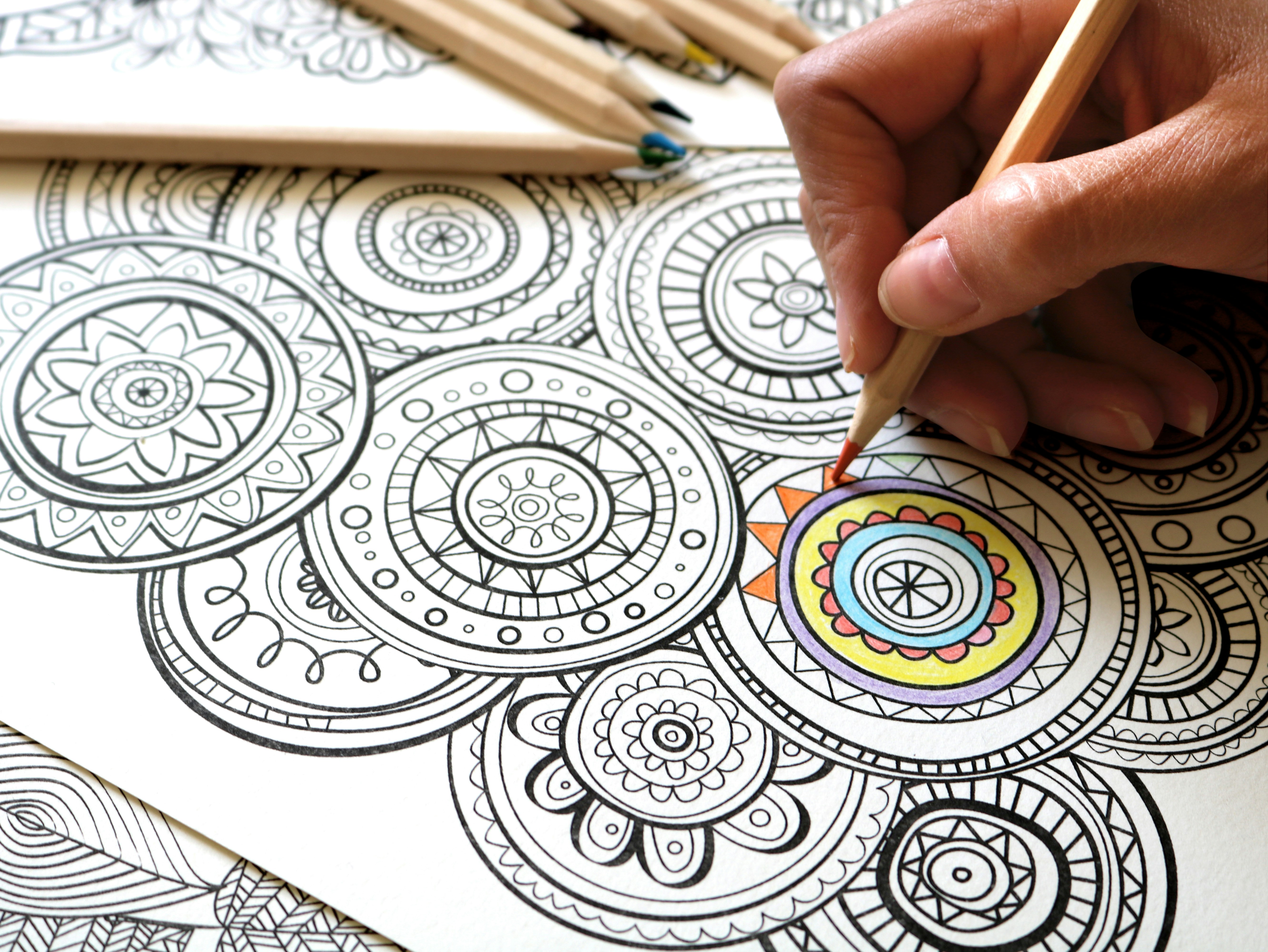 Image of a hand holding a colouring pencil, filling up colours for a pattern colouring sheet